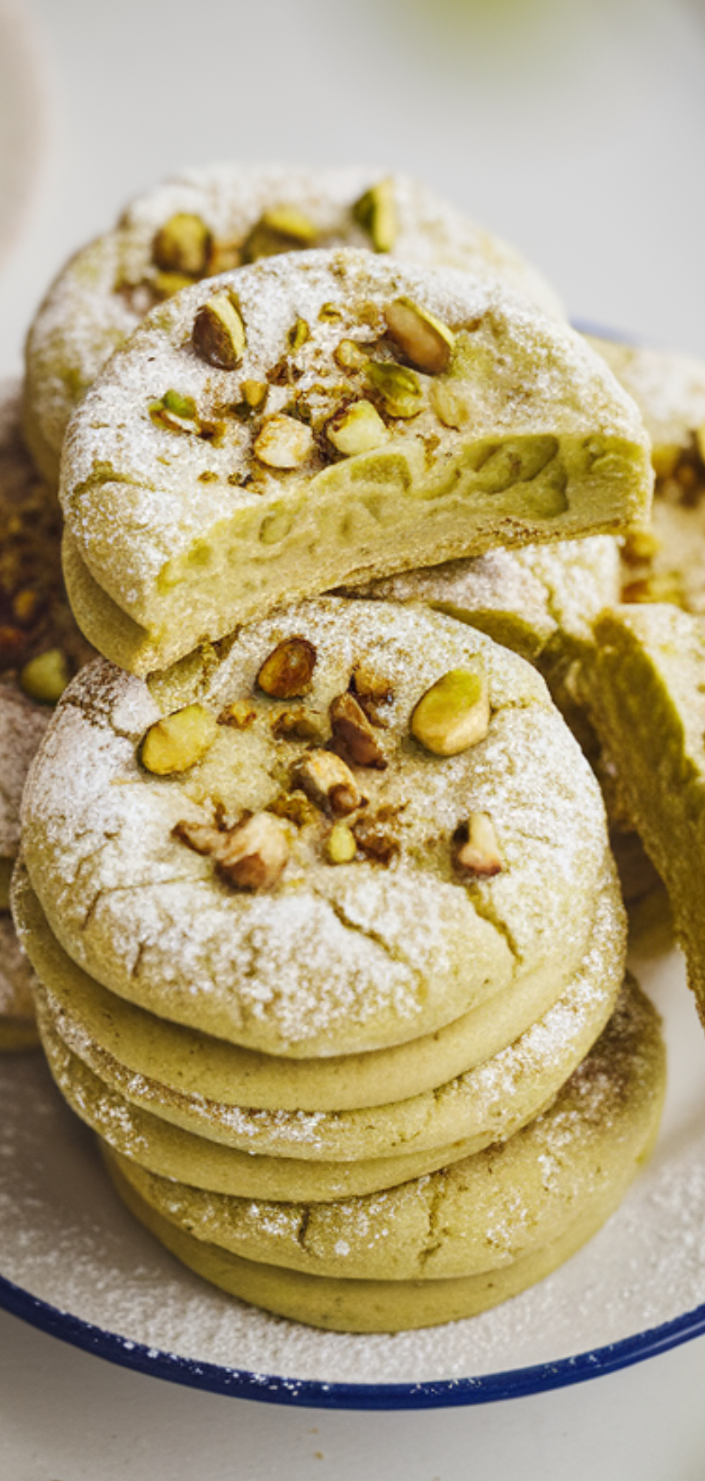 "A plate of green-tinted pistachio pudding cookies with one cookie broken in half showing the soft inside."