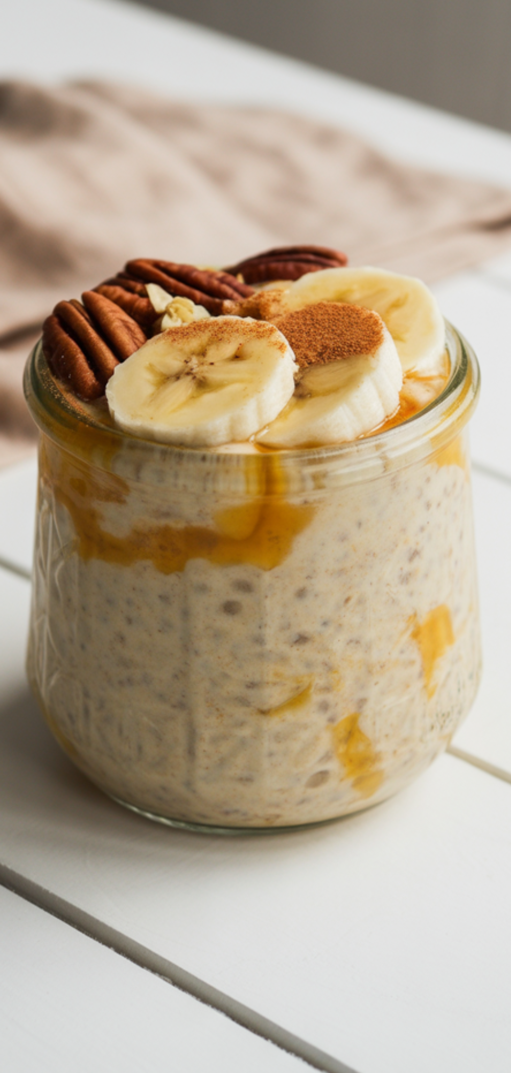 Close-up of overnight oats with pumpkin purée and granola served in a clear jar on bright background.