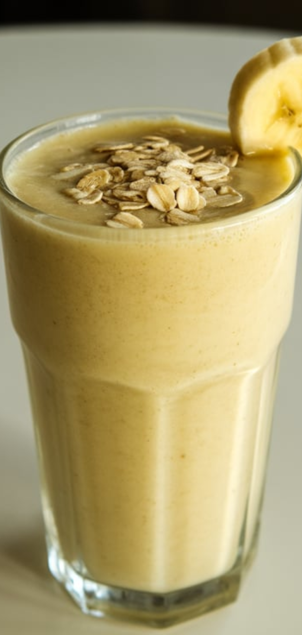 "A tall glass of bright green morning energy smoothie on a white table, topped with chia seeds and banana slices, with natural daylight lighting."