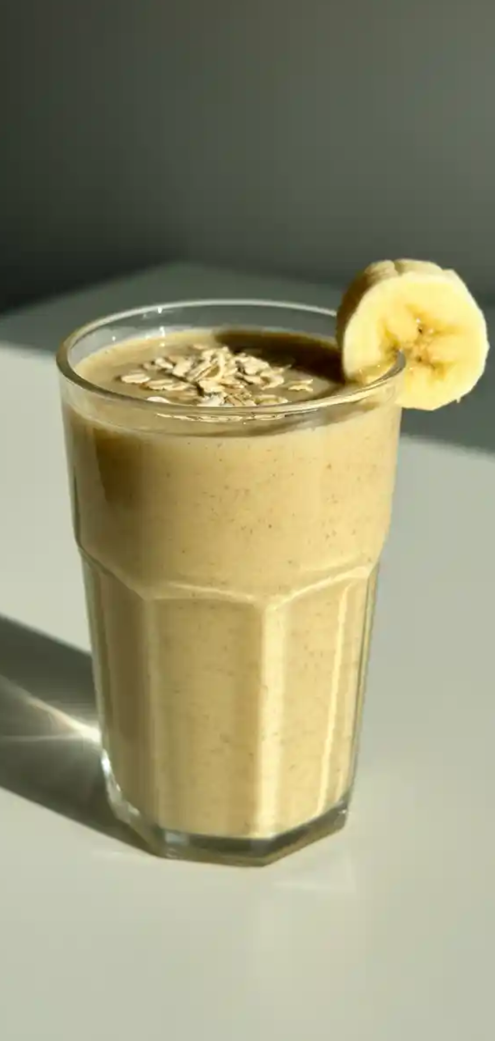 "Vibrant green smoothie served in a clear glass jar with reusable straw, surrounded by fresh ingredients like spinach, banana, and oats."