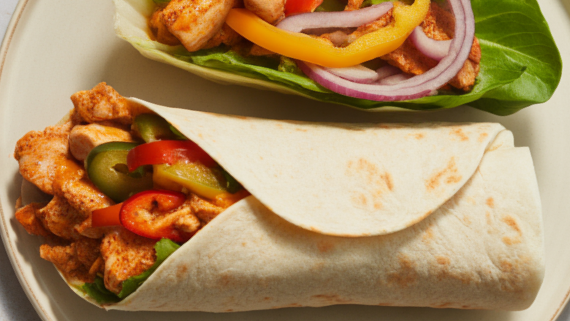 Chili Chicken Wrap on a white plate with tender chicken strips, colorful bell peppers, onions, and fresh lettuce, slightly open to show filling, with a small bowl of chili sauce on the side, bright natural lighting, food blogger style