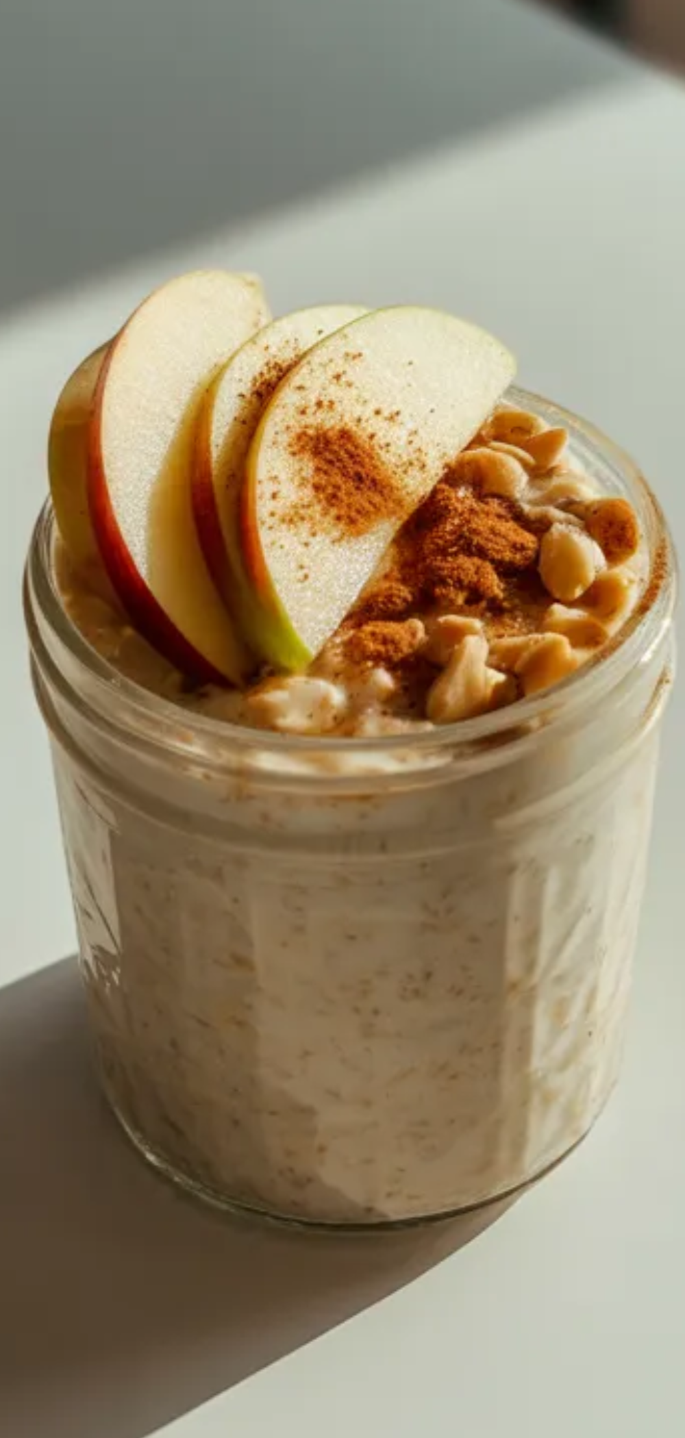 Creamy apple cinnamon overnight oats with honey and cinnamon served in a jar on a white table styled like a food blogger breakfast scene