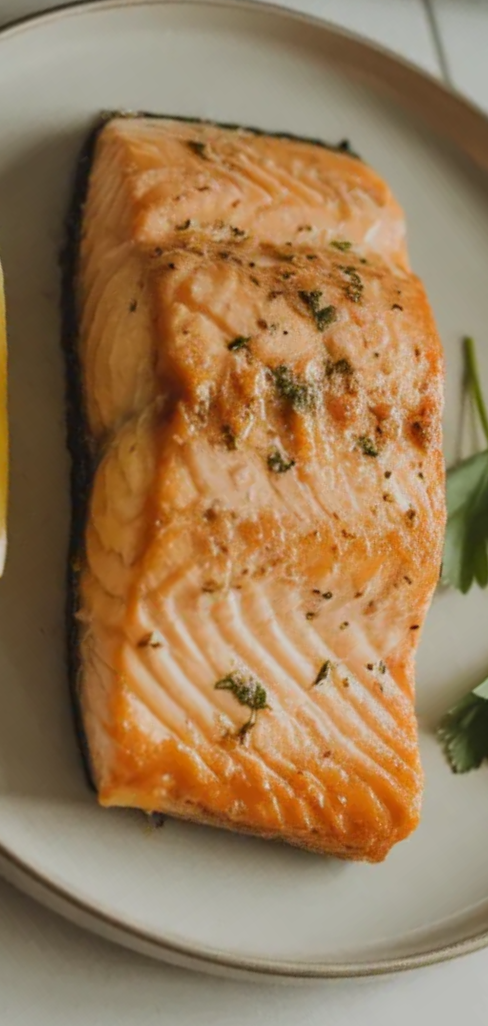 Crispy golden salmon fillet made in an air fryer served on a clean white table with soft natural lighting and a fresh herb garnish.