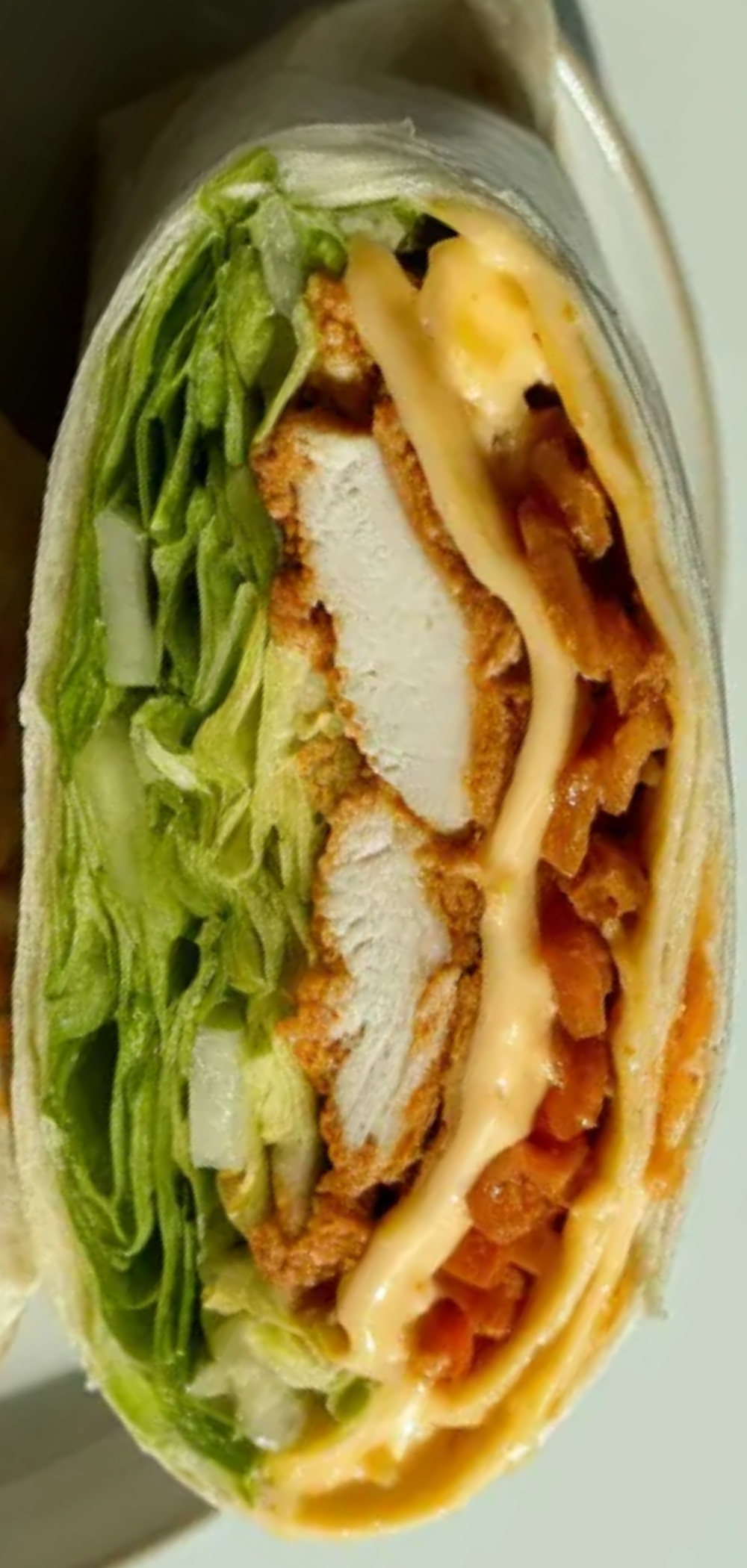 Crispy golden tortilla wrap filled with chicken, cheese, and fresh veggies, placed on a clean white table for a simple and appetizing look.