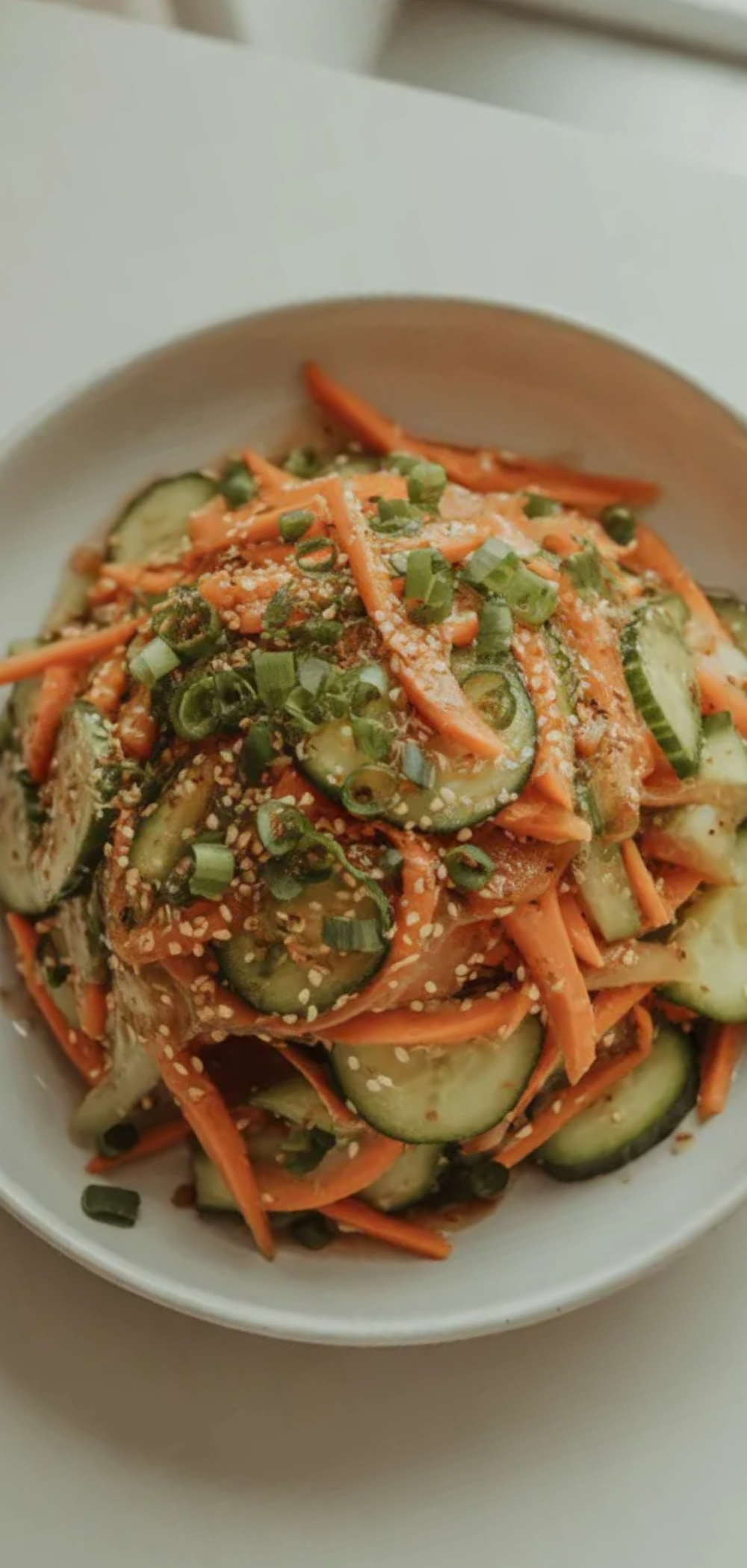 Fresh carrot and cucumber salad with sesame dressing served in a minimal white bowl bright natural lighting