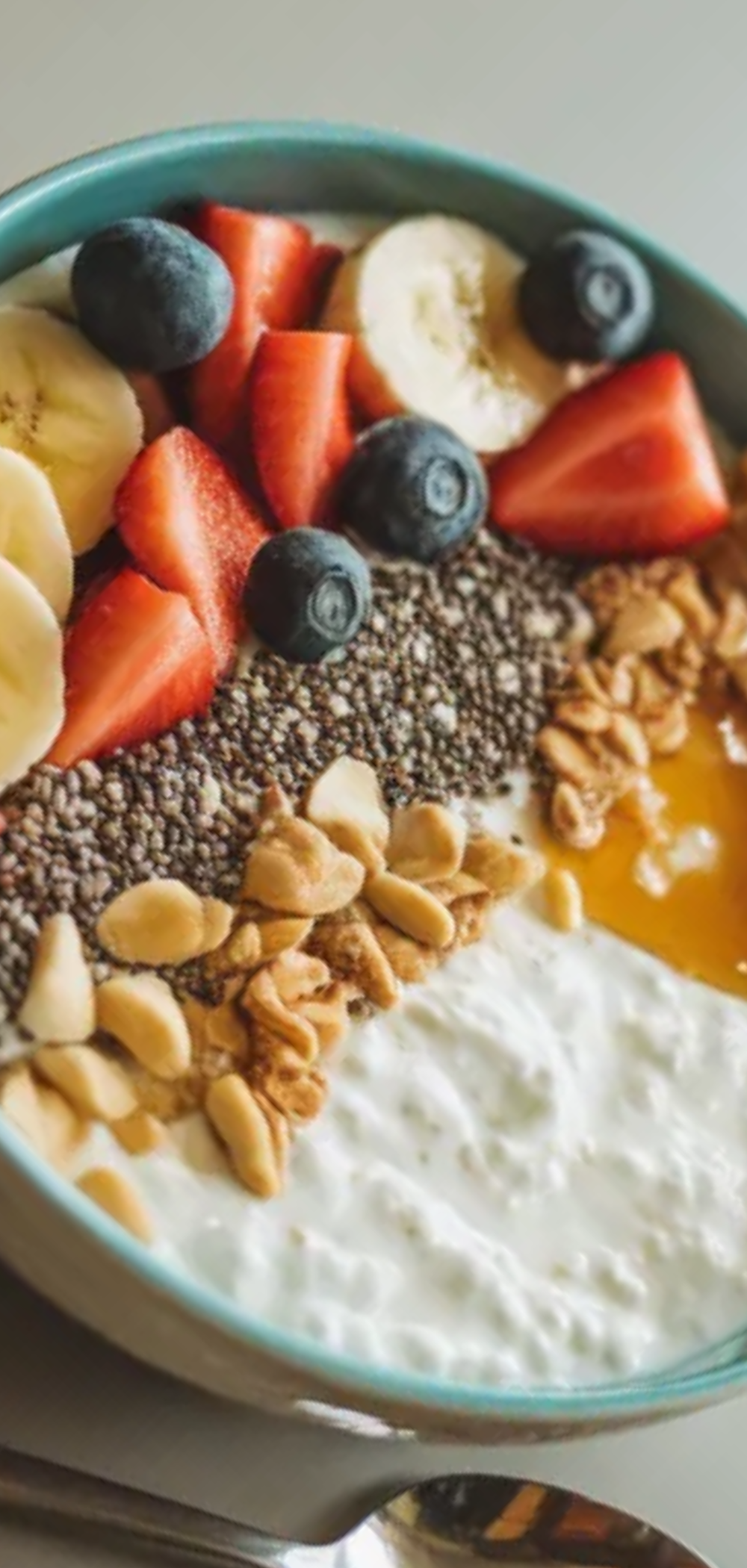 Close-up of a creamy cottage cheese breakfast bowl with colorful fruit, crunchy granola, and a drizzle of honey, served with a spoon on the side.