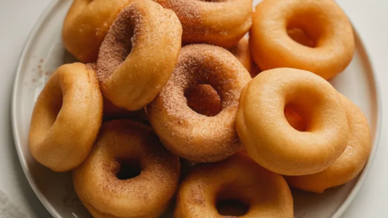 “Plate of golden-brown air fryer donuts dusted with cinnamon sugar on a white table with donut holes scattered around, shot in natural daylight”