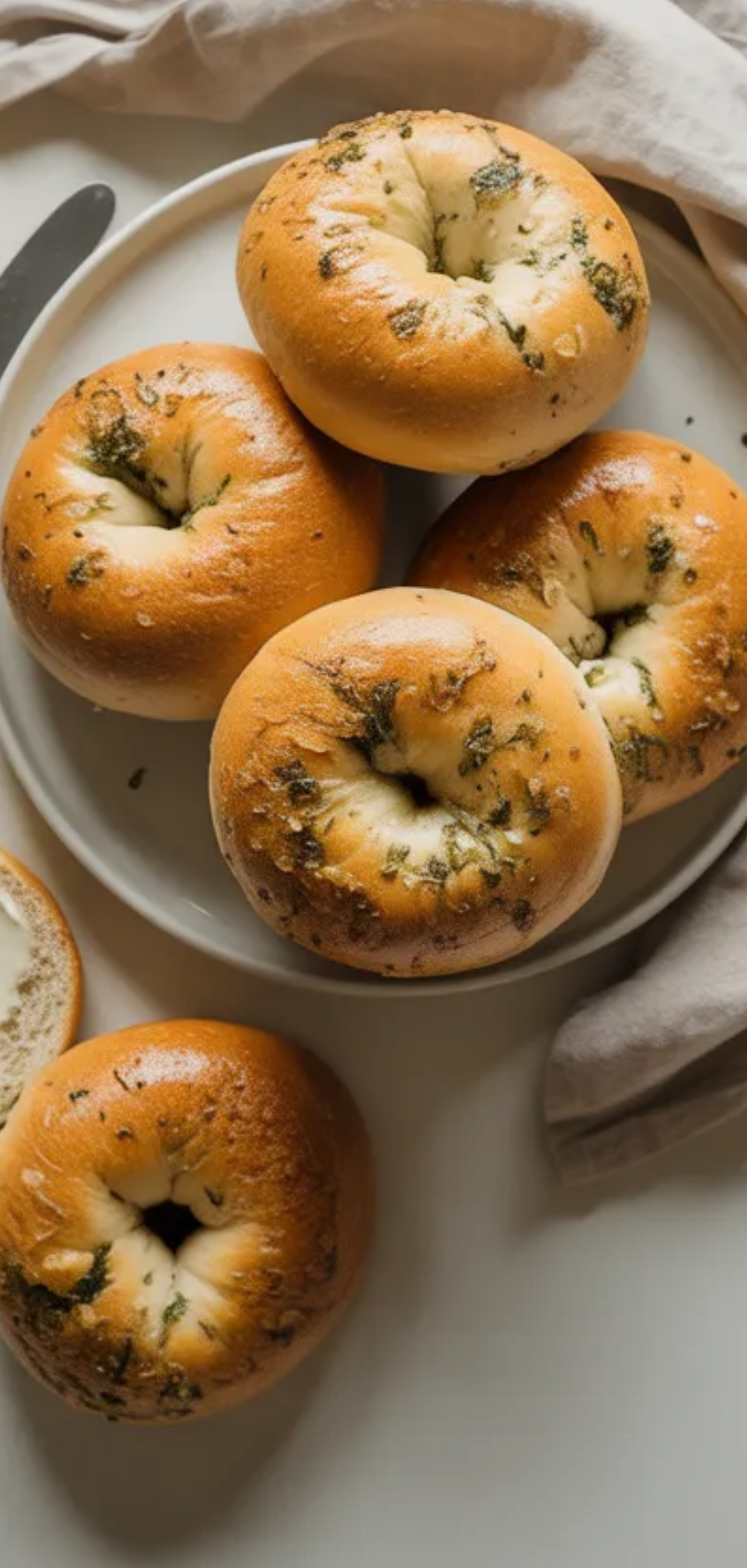 Freshly baked garlic herb bagels with visible herbs and a soft interior served on a minimal white background