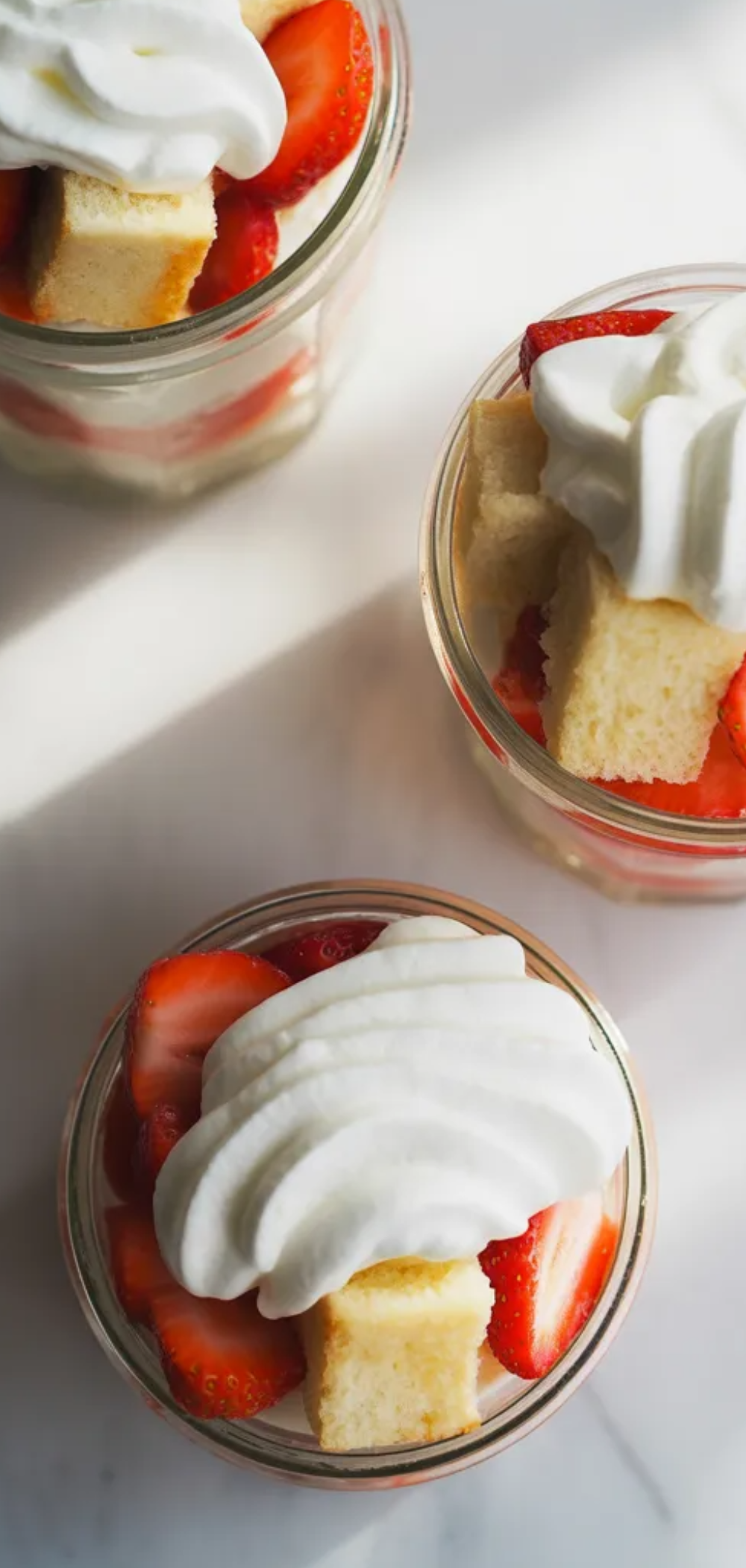 Food blogger style photo of strawberry shortcake jars arranged neatly on a white table with natural light and soft, realistic textures.

