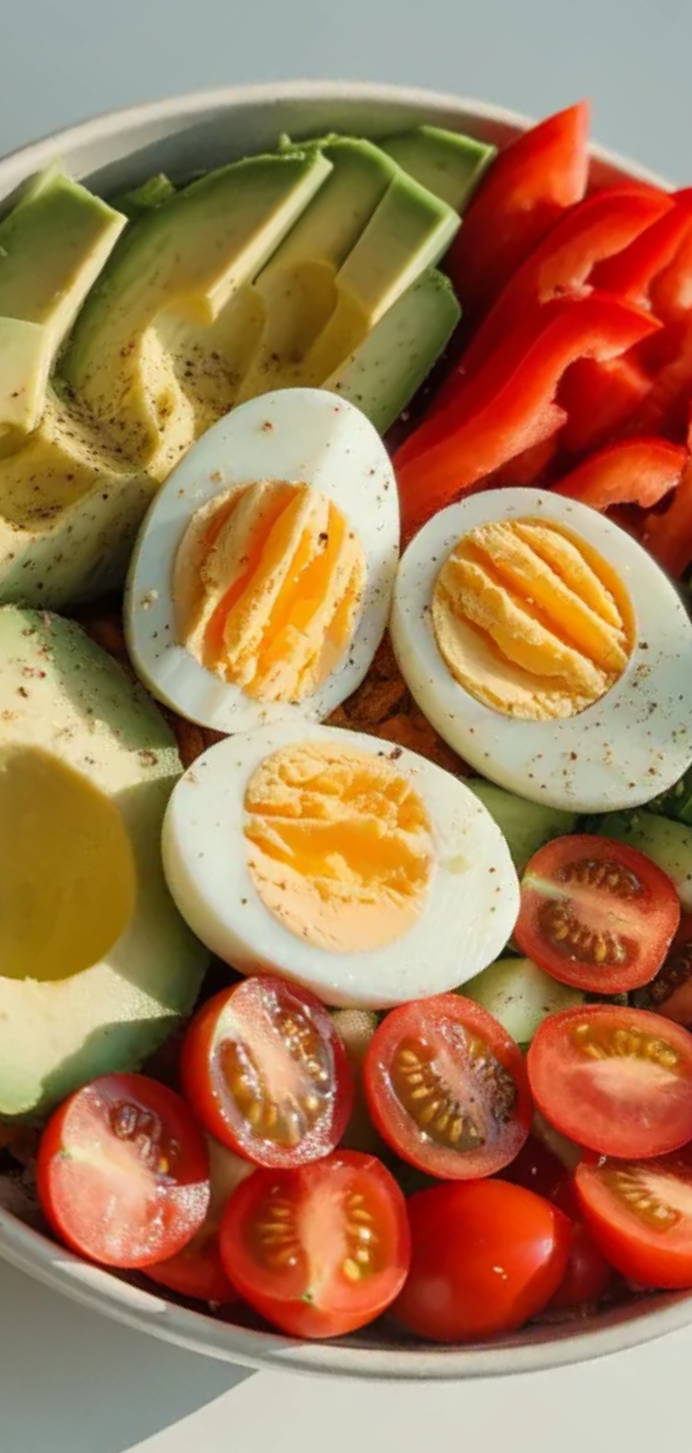 “Healthy breakfast bowl with creamy avocado, sliced eggs, and fresh colorful vegetables in a white bowl.”