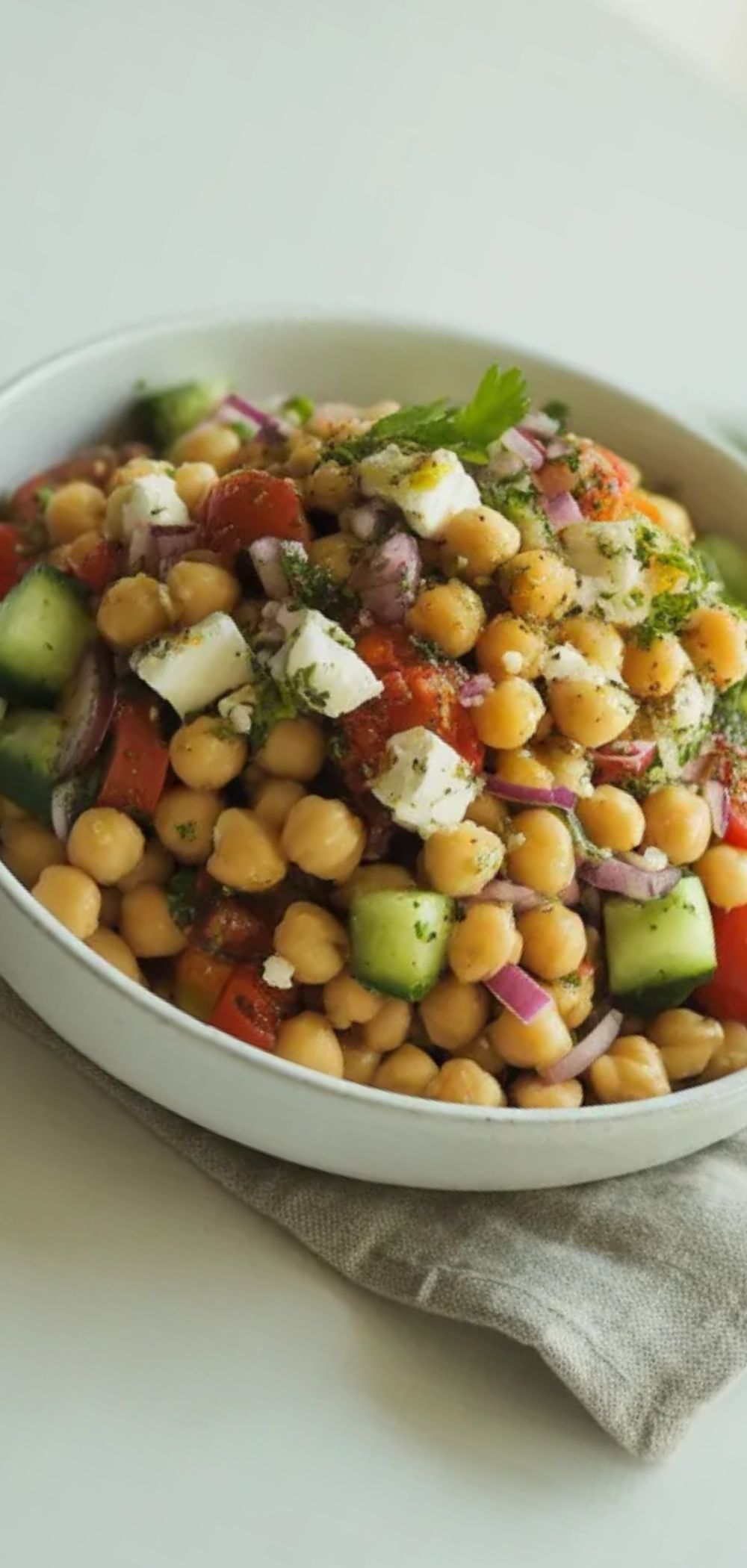 Easy Mediterranean salad made with chickpeas, cherry tomatoes, cucumber, and feta cheese, styled on a bright white background