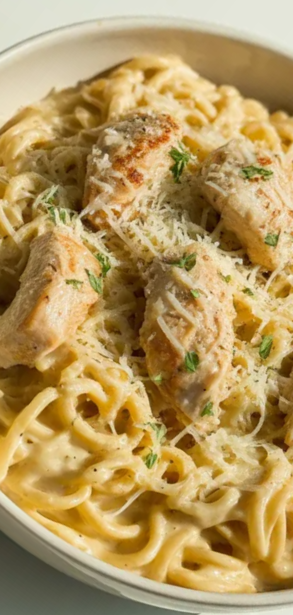 Close-up of cheesy chicken Alfredo pasta served in a bowl with tender chicken pieces and garnished with parsley, food blogger style.