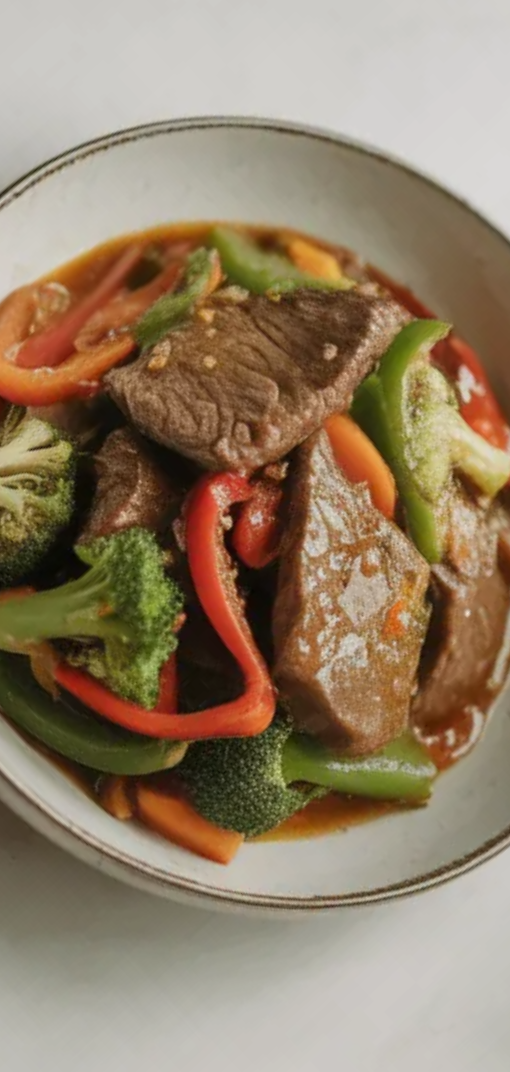 Close-up of healthy beef stir fry with tender beef strips, broccoli, bell peppers, and carrots in a light sauce served in a white bowl on a clean white table