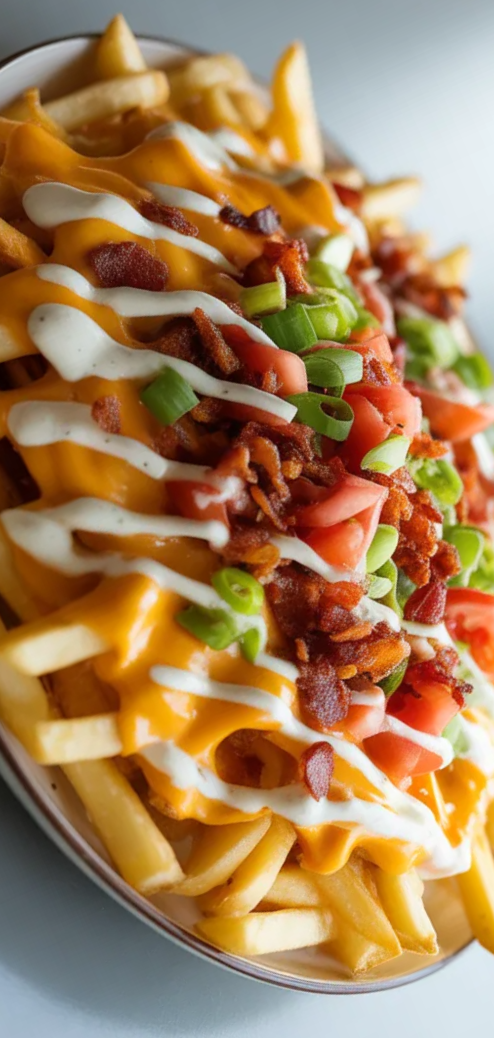 “Close-up of cheesy loaded fries with bacon, fresh veggies, and creamy sauce, served on a clean white surface in natural daylight.”