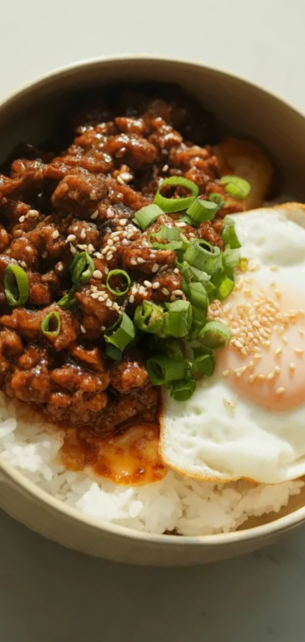 Close-up food photo of a Korean-inspired beef rice bowl with glazed ground beef, white rice, sesame seeds, and chopped green onions, styled like a clean food blogger shot with bright natural light.