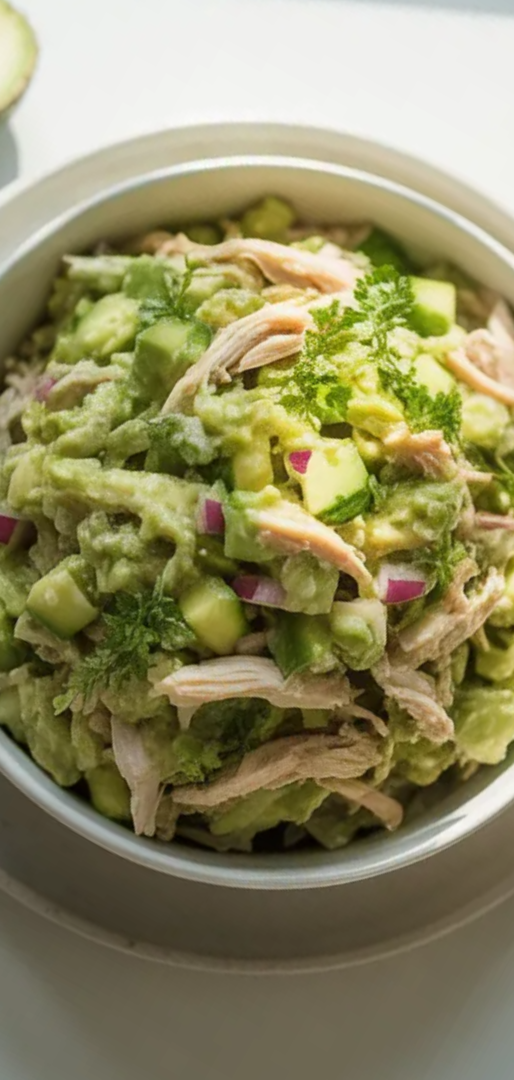 A fresh homemade creamy avocado chicken salad in a white ceramic bowl, styled on a bright white table with soft natural lighting.