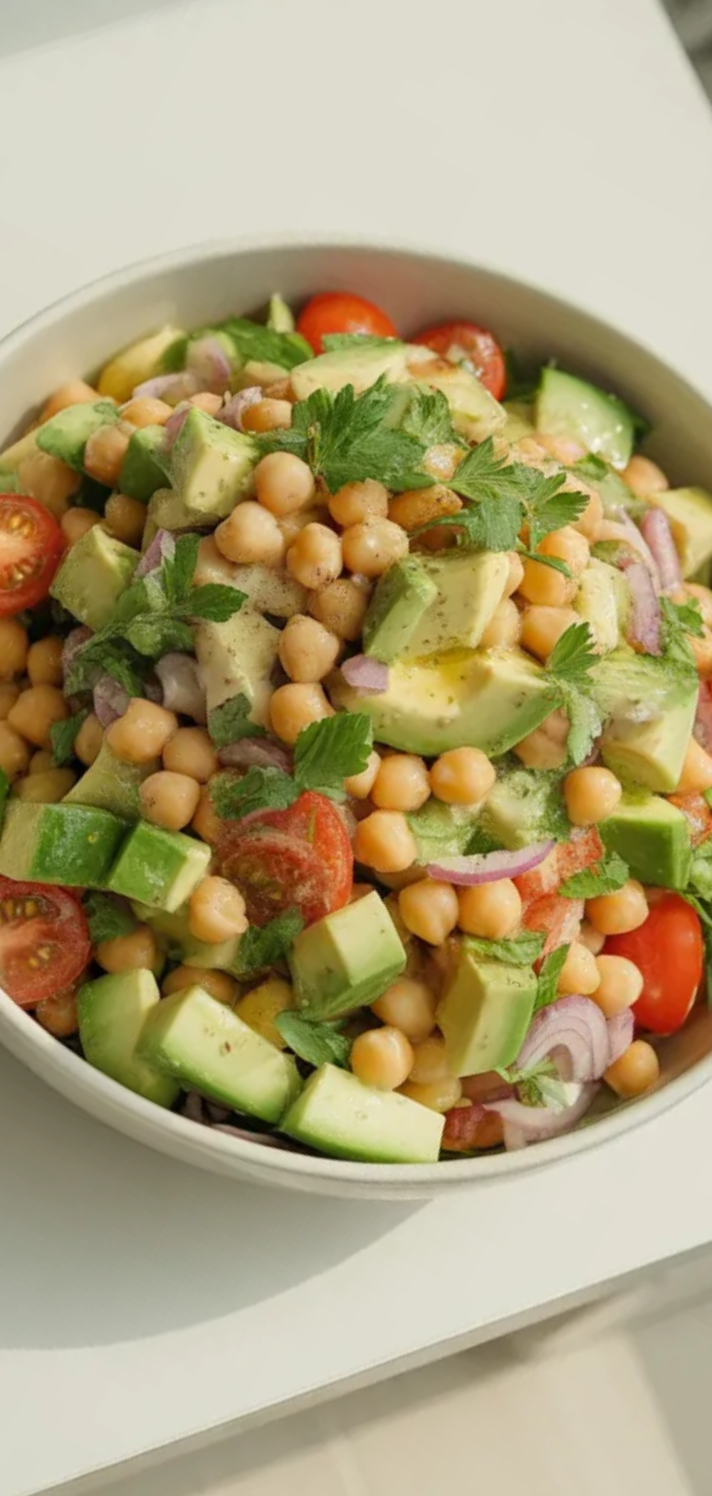 Healthy chickpea avocado salad with cucumber, tomatoes, and red onion in a clean food blogger style
