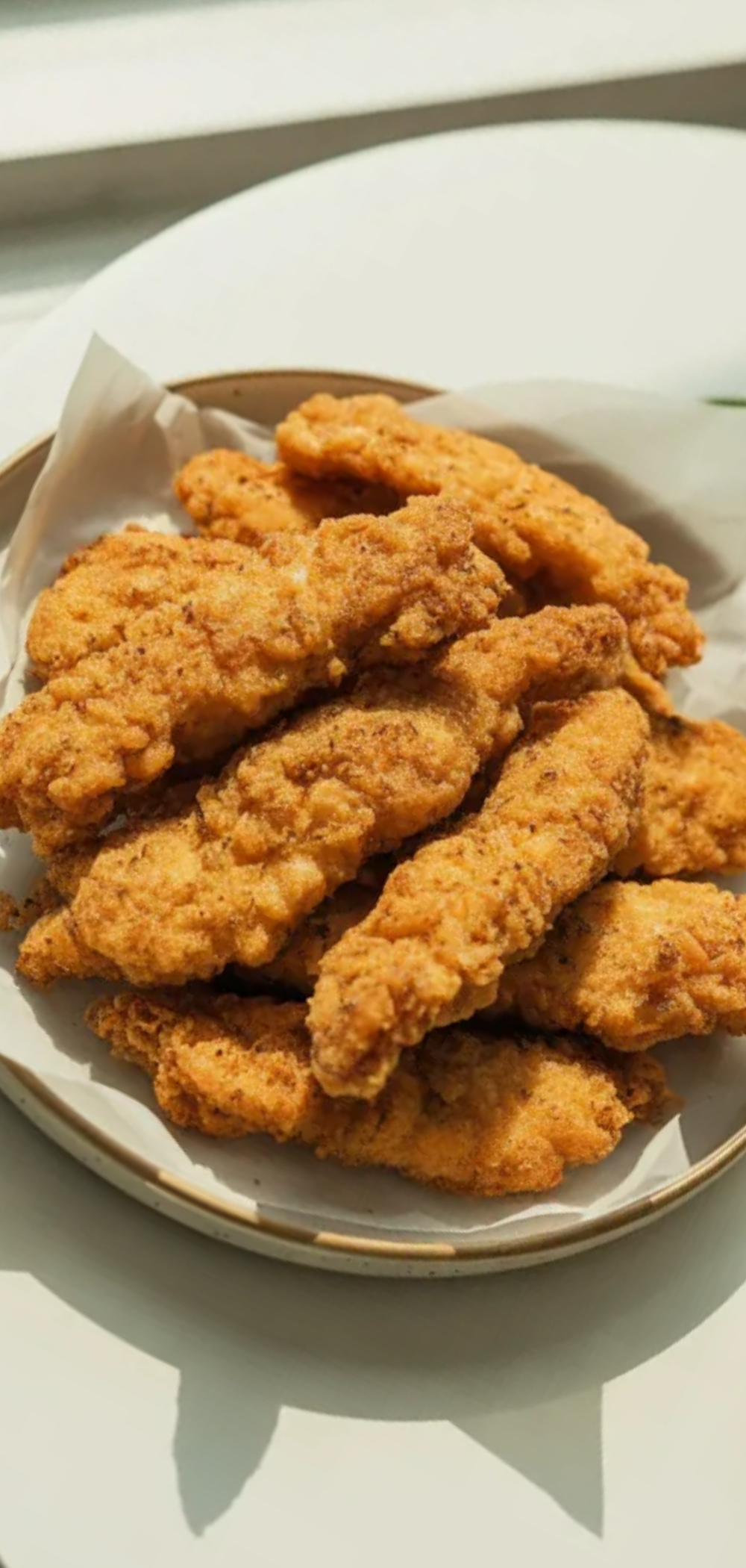 Homemade crispy chicken strips with crunchy coating, plated neatly with sauce, styled on a bright minimalist food photography background