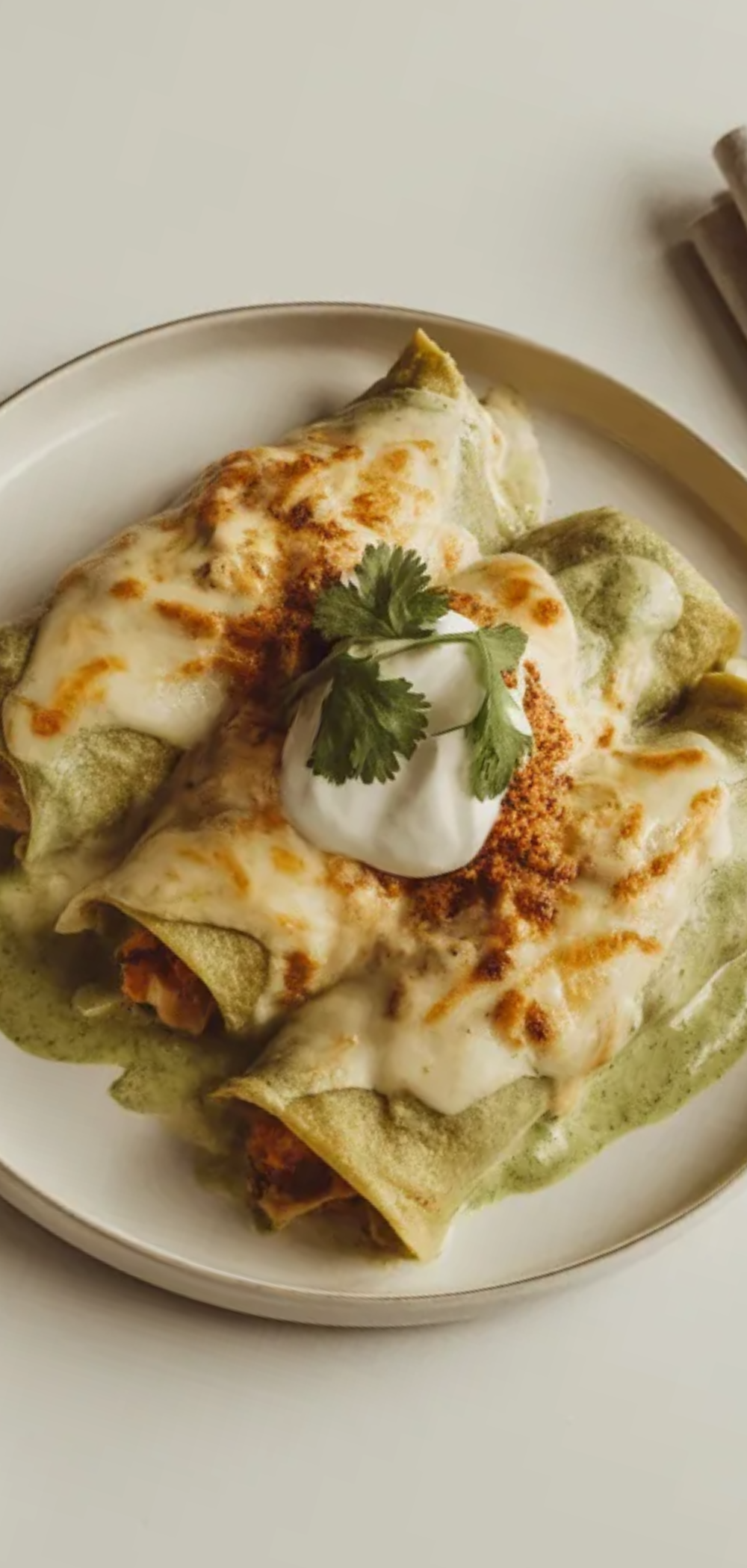 Close up of homemade green chicken cream cheese enchiladas with creamy sauce and melted cheese on a clean white table