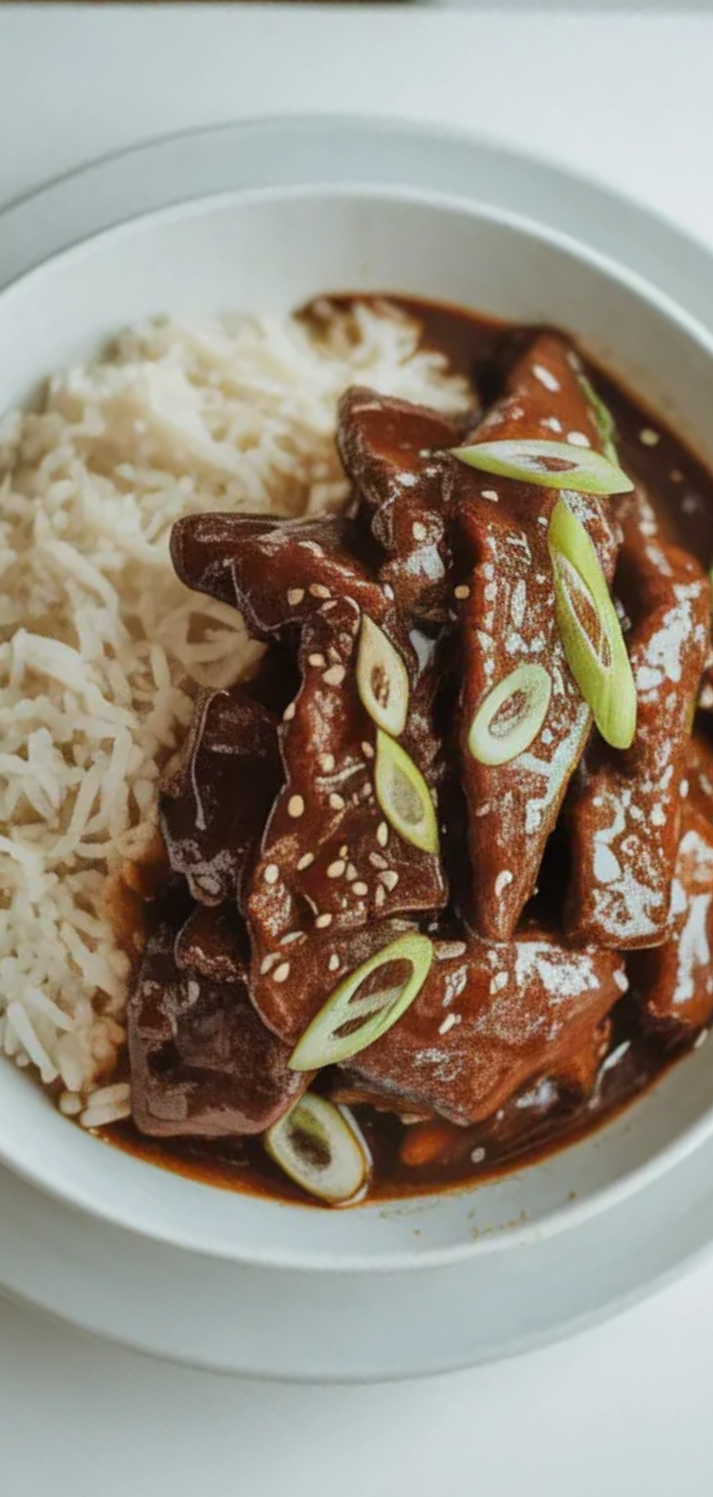 Restaurant-style Mongolian Beef with shiny sauce, sesame seeds, and green onions served with rice in a bright minimal food photography setup.