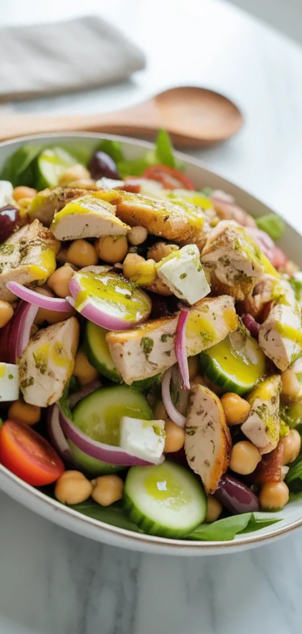 Fresh Mediterranean-style Greek salad with grilled chicken, chickpeas, vegetables, and feta cheese, served in a white bowl on a minimal white background with soft natural lighting.