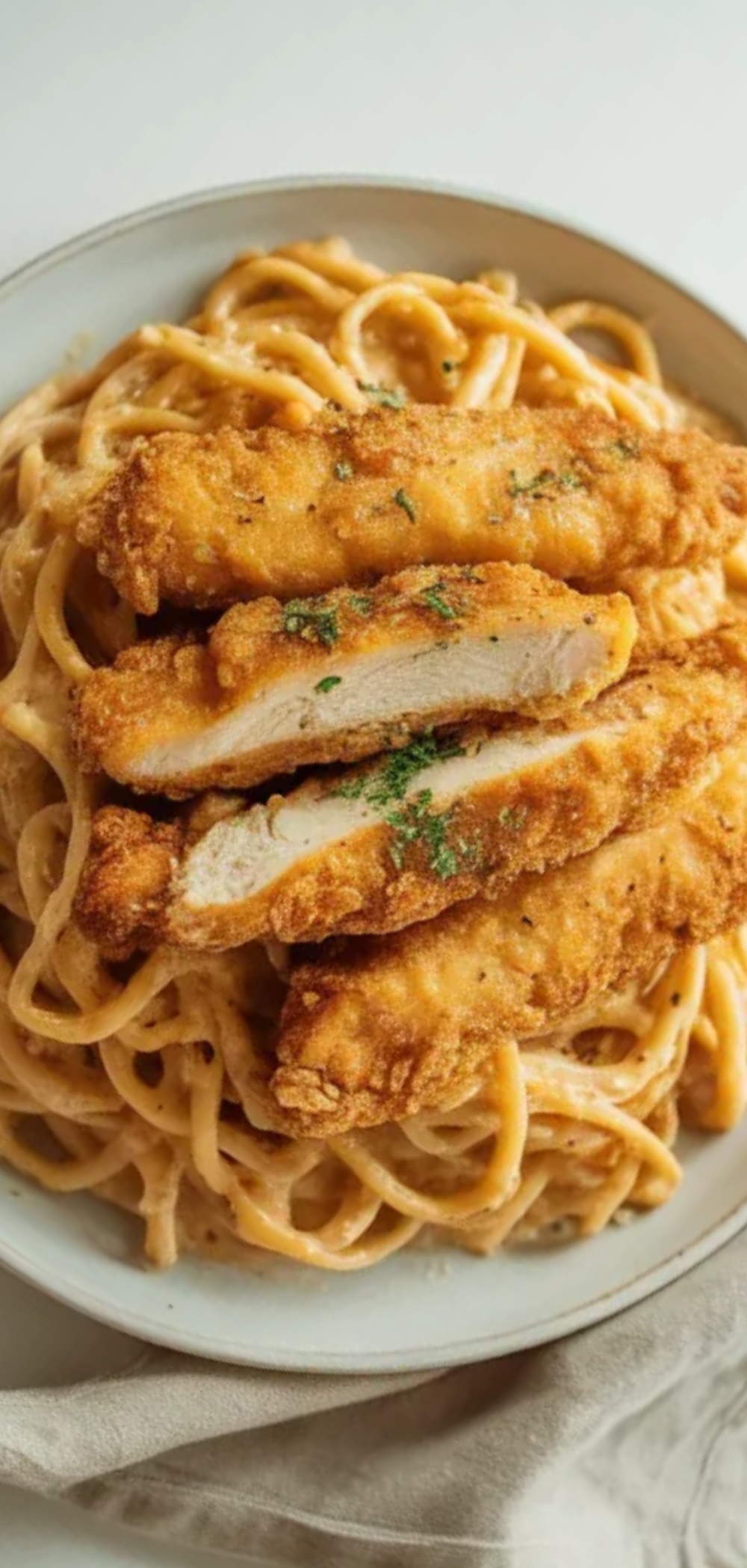 food photo of creamy pasta topped with crunchy fried chicken, served on a clean white table with soft natural lighting.