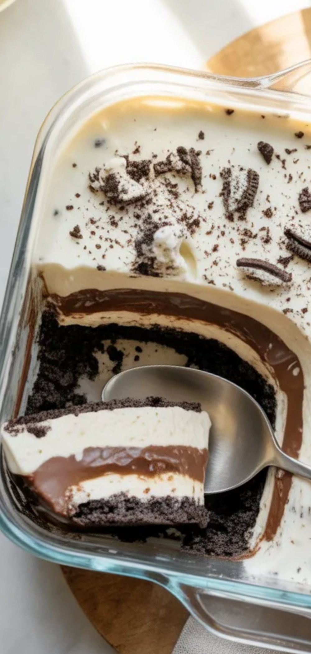 Homemade no-bake Oreo dessert with visible layers of cookies, cream cheese filling, and chocolate pudding topped with whipped cream and Oreo crumbs.