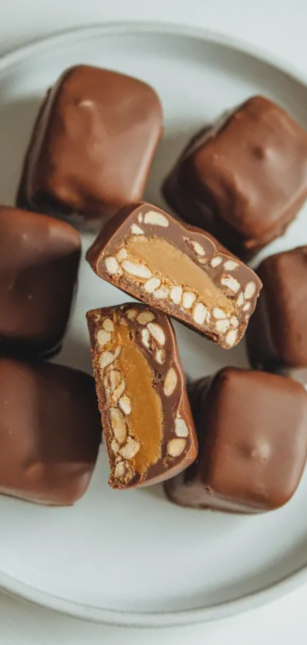 Homemade healthy date snickers with creamy peanut butter and chocolate coating on a clean white table