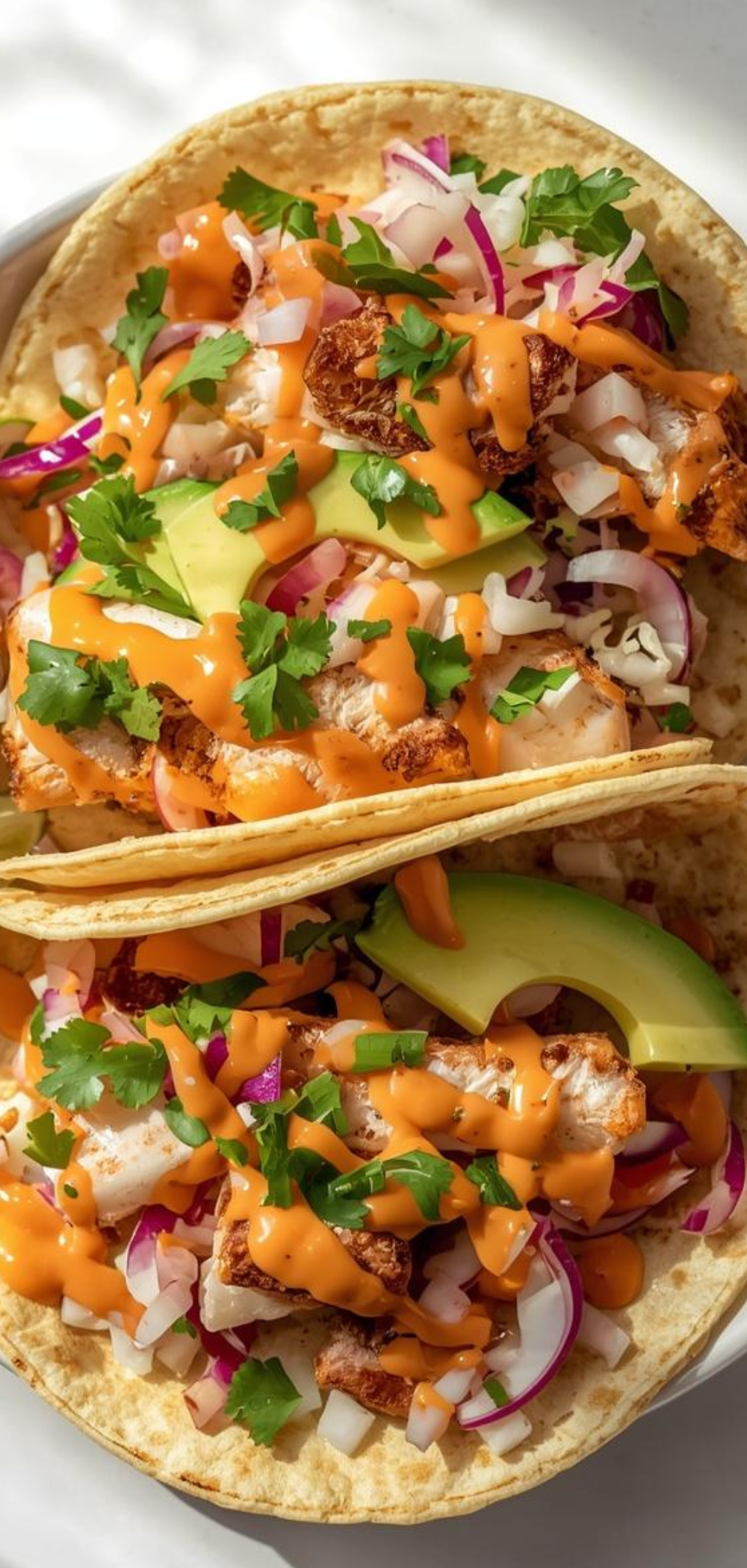 Close-up of colorful fish tacos topped with cilantro, red onion, and lime wedges, arranged neatly on a plate with soft natural lighting.