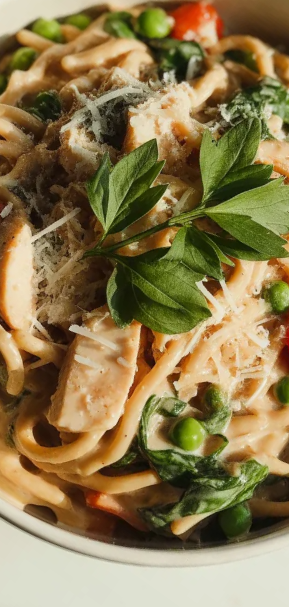 “Colorful protein-packed pasta served on a bright white table, topped with cherry tomatoes, peas, spinach, and grated cheese”