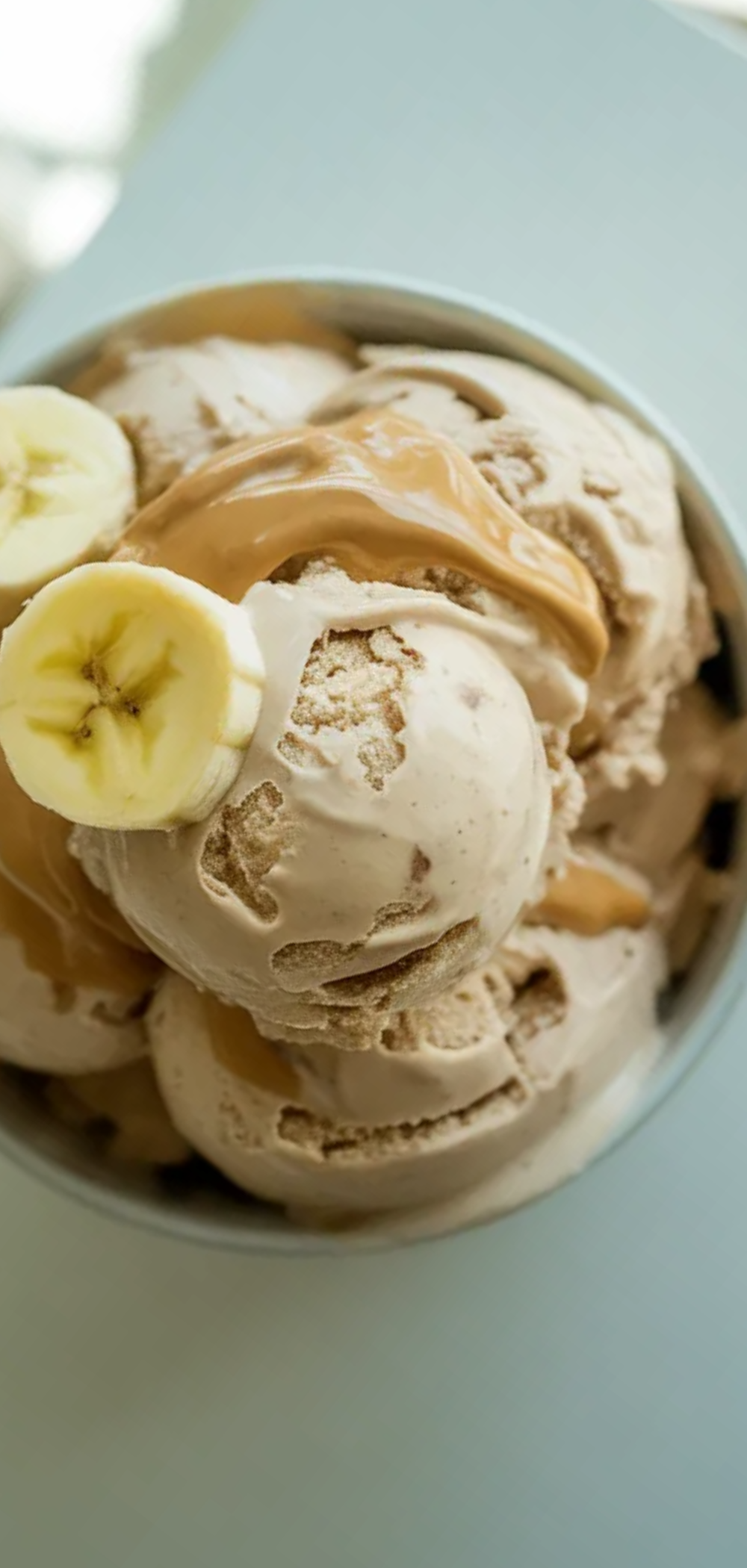 Healthy banana protein ice cream with a smooth texture topped with fresh banana slices and peanut butter on a bright white background