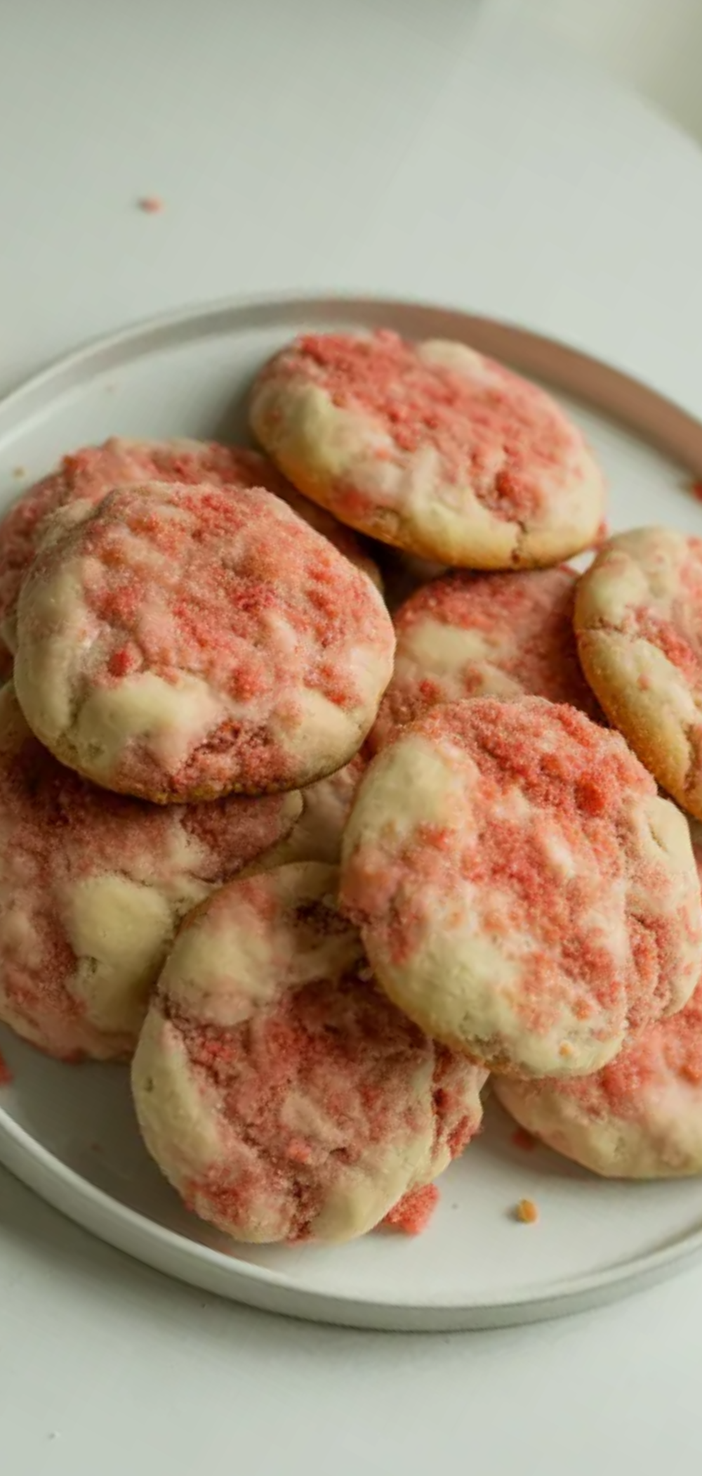 Alt Text: Homemade strawberry crunch cookies with pink crumb coating, scattered cookie crumbs, white minimal background, authentic food blogger style