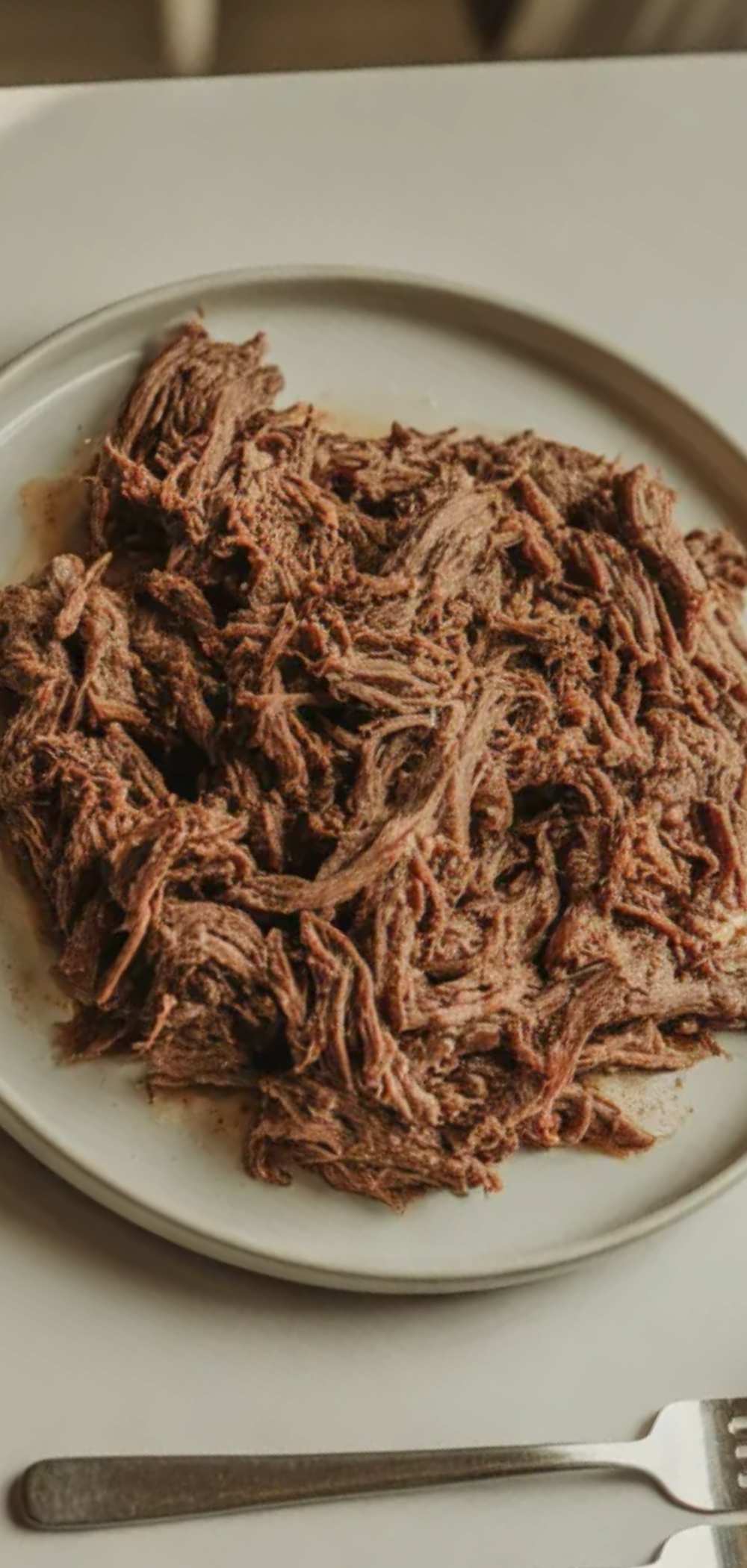 Tender slow cooker beef pulled apart with forks on a clean white background