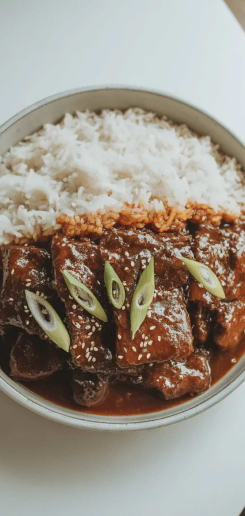 A bowl of Mongolian Beef served with white rice on a clean white table.