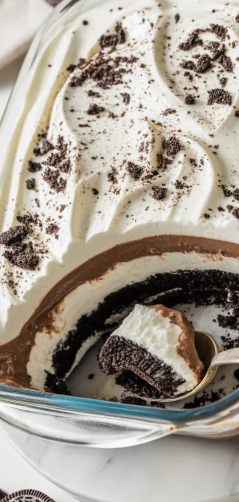 A chilled Oreo layered dessert served in a glass pan, showing creamy textures and crushed cookie topping on a bright white food photography background.