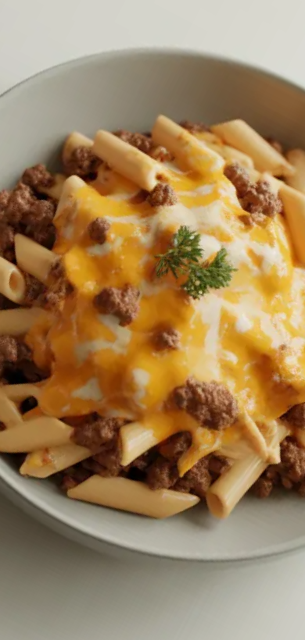 One pan cheesy beef pasta topped with parsley in a modern white bowl, realistic texture, soft light, simple clean setup