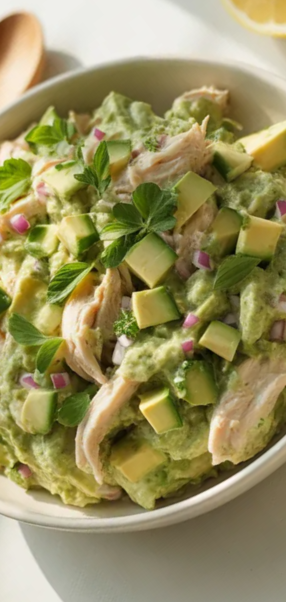 A creamy avocado chicken salad served in a white bowl with fresh diced vegetables, seen on a clean white table with natural light.