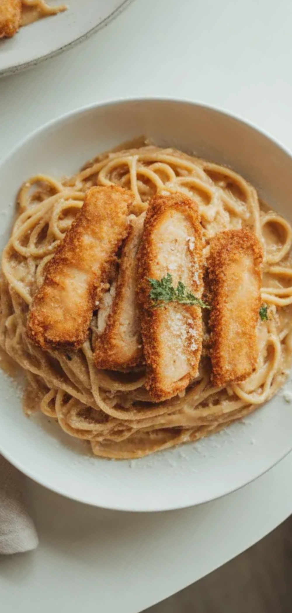 Homemade crispy chicken with rich creamy pasta served in a white dish, styled like a food blog recipe photo with minimal shadows and fresh garnish.