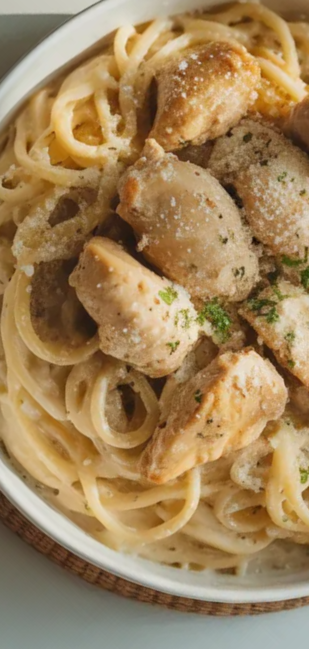 Homemade one-pot chicken Alfredo pasta with creamy sauce, chicken chunks, and Parmesan cheese, styled on a white table with soft natural lighting.
