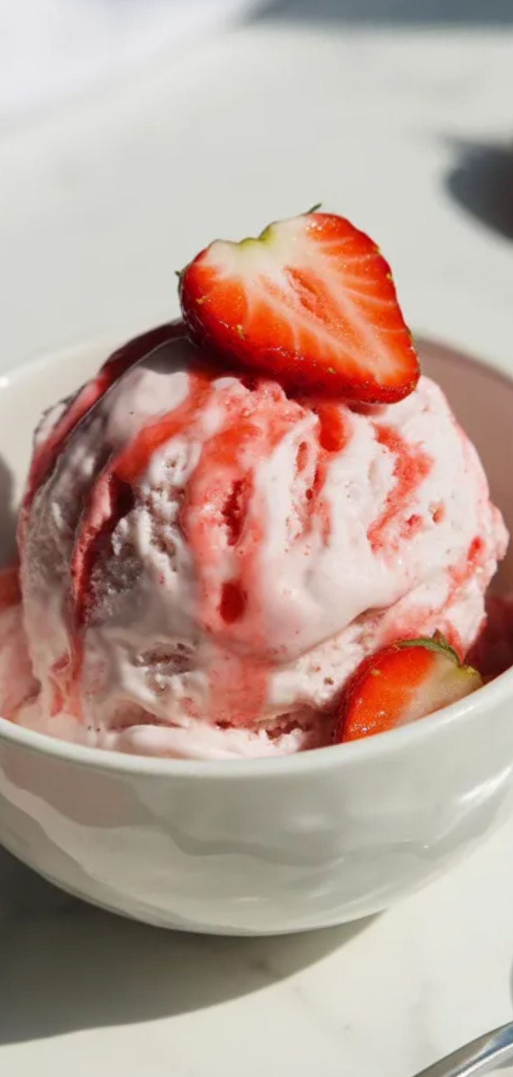 Creamy homemade strawberry cottage cheese ice cream in a white bowl with soft shadows, fresh strawberries around and a simple modern food blogger setup