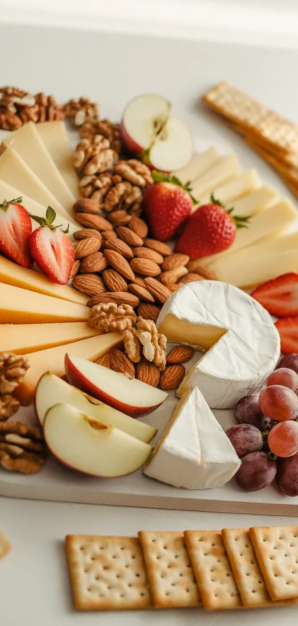 Colorful snack board featuring cheddar, brie, fresh fruits, nuts, and crackers, photographed in soft natural daylight.
