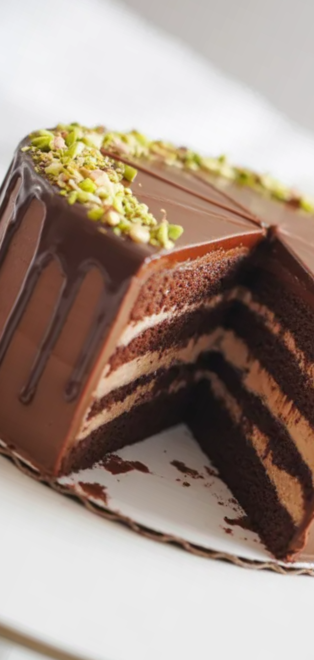 Luxury chocolate cake inspired by Dubai desserts topped with pistachios and smooth ganache on a white table with soft lighting

