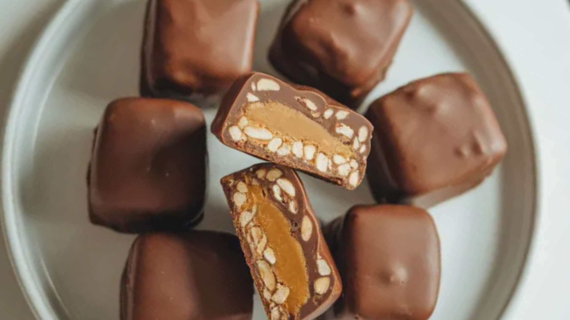 Chocolate-covered date snickers filled with peanut butter and topped with chopped peanuts on a white plate