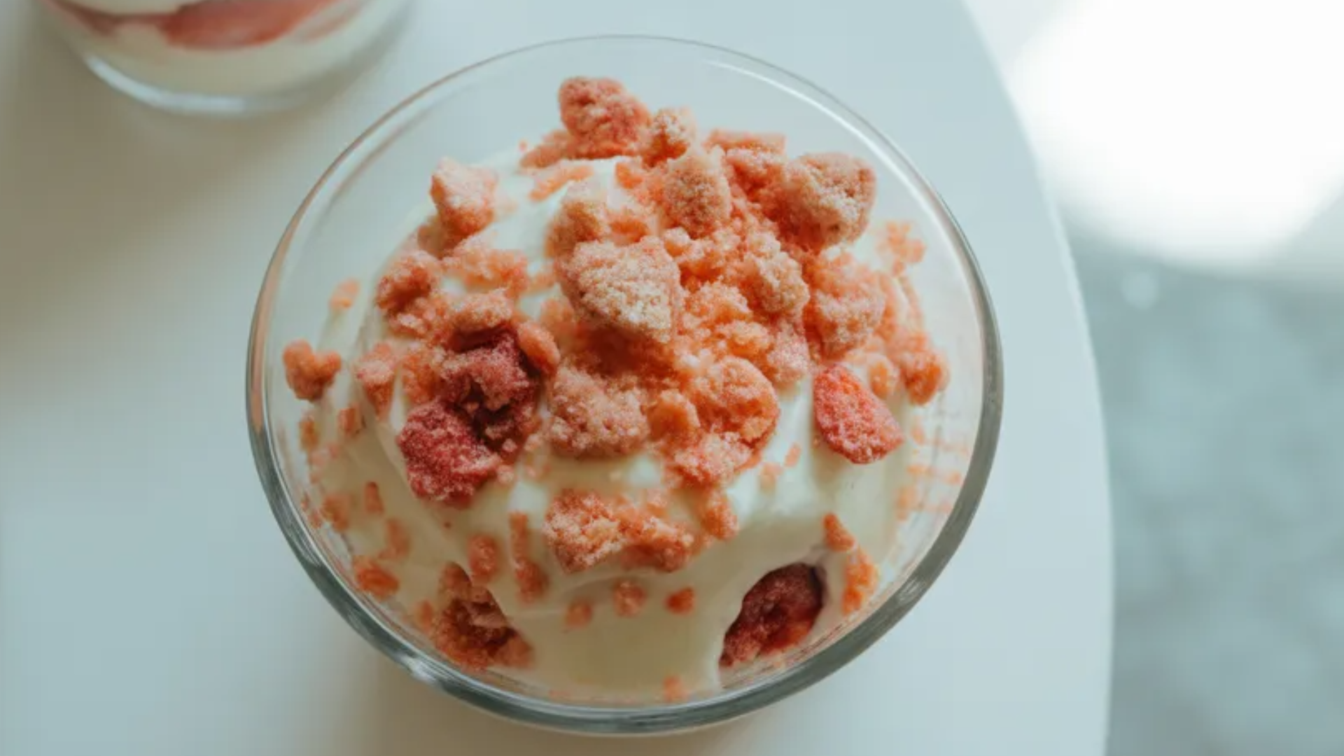 Strawberry crunch cups in clear glasses layered with creamy filling, fresh strawberries, and crunchy cookie topping on a white table