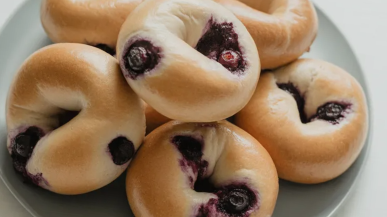 Fresh homemade blueberry bagels on a white table with bright lighting and no shadows, showing soft texture and real blueberries inside