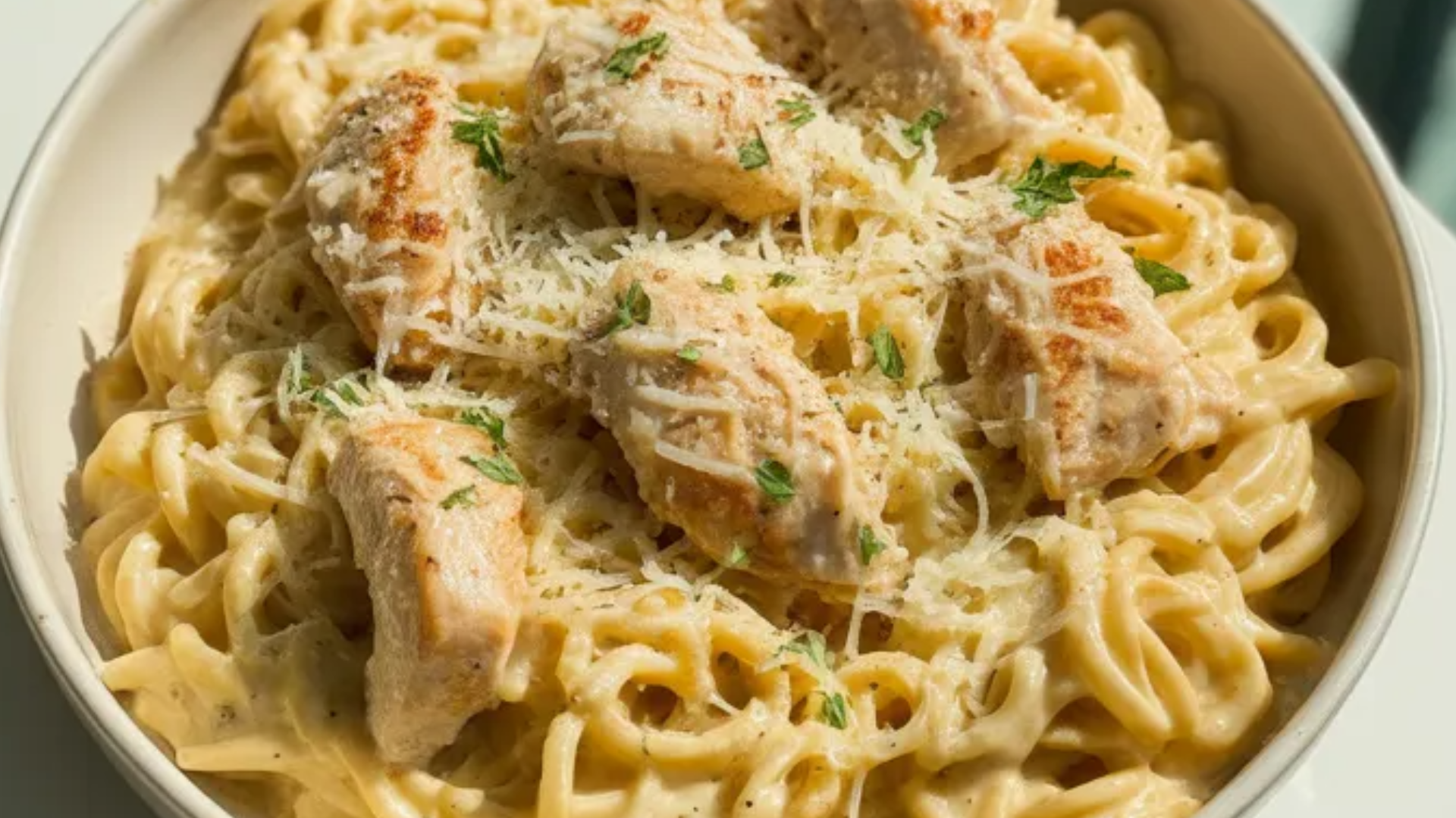 Creamy one-pot chicken Alfredo pasta in a white bowl, topped with Parmesan cheese and fresh parsley on a bright white table.