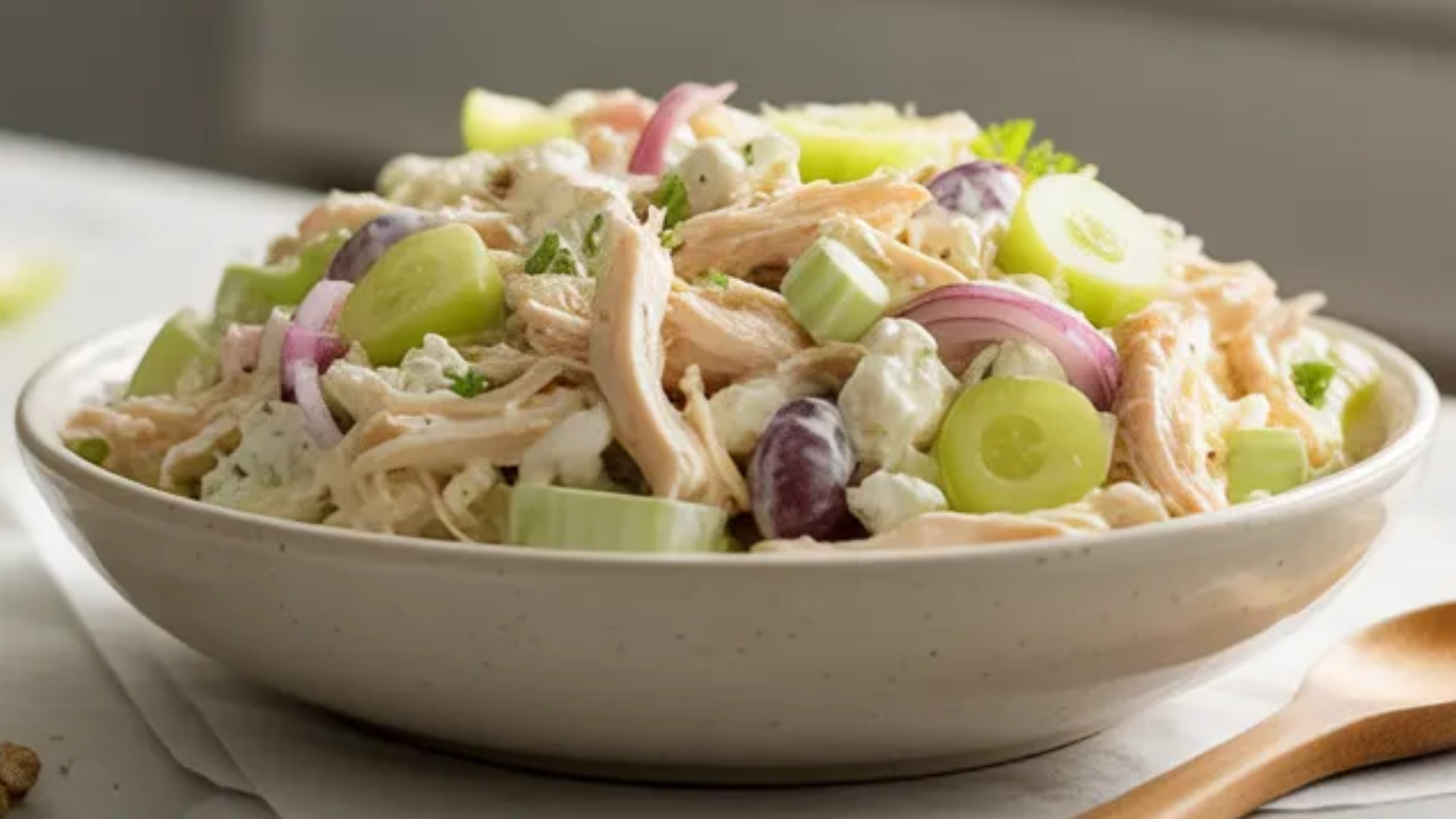 Creamy cottage cheese chicken salad in a white bowl with shredded chicken, celery, red onion, and grapes on a white marble table with soft natural light