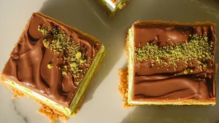 Pistachio Kunafa Chocolate Bars cut into squares showing layers of crispy golden kunafa, green pistachio cream, and glossy chocolate topping on a white marble table.