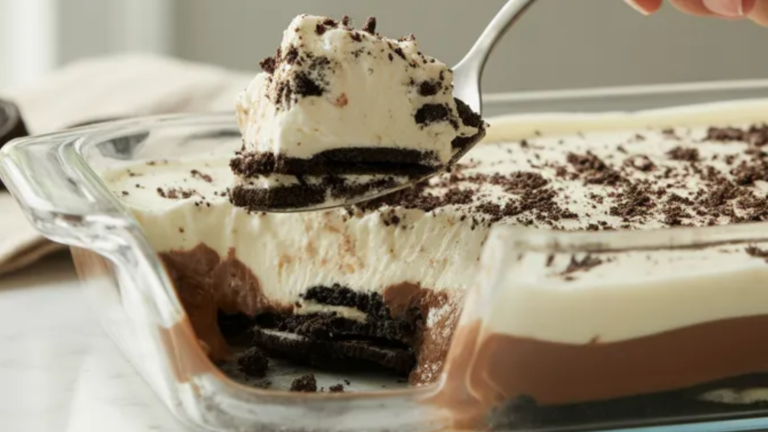 A layered no-bake Oreo dessert in a glass dish showing crushed Oreo crust, creamy cheesecake layer, chocolate pudding, and whipped topping with crushed Oreos on top.