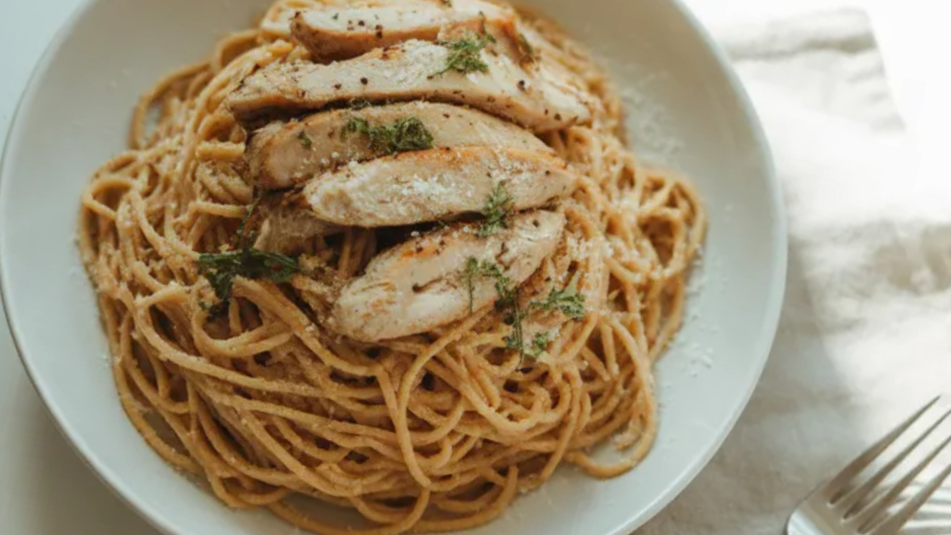Creamy protein pasta with grilled chicken and parmesan served in a white bowl on a clean white table with natural light